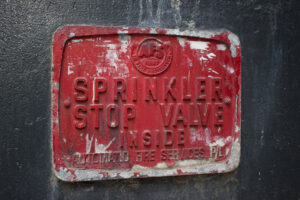 Photo of an old red metal sign with 'Sprinkler Stop Valve Inside' in writing.