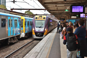 People waiting on a platform at Flinders Street Station while a purple V/LIne Vlocity train arrives next to a blue Metro Trains train.