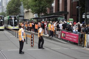 Photo of a crowded tram stop platform with Yarra Trams staff in orange hi viz vests during the 2025 Australian Grand Prix in Melbourne.